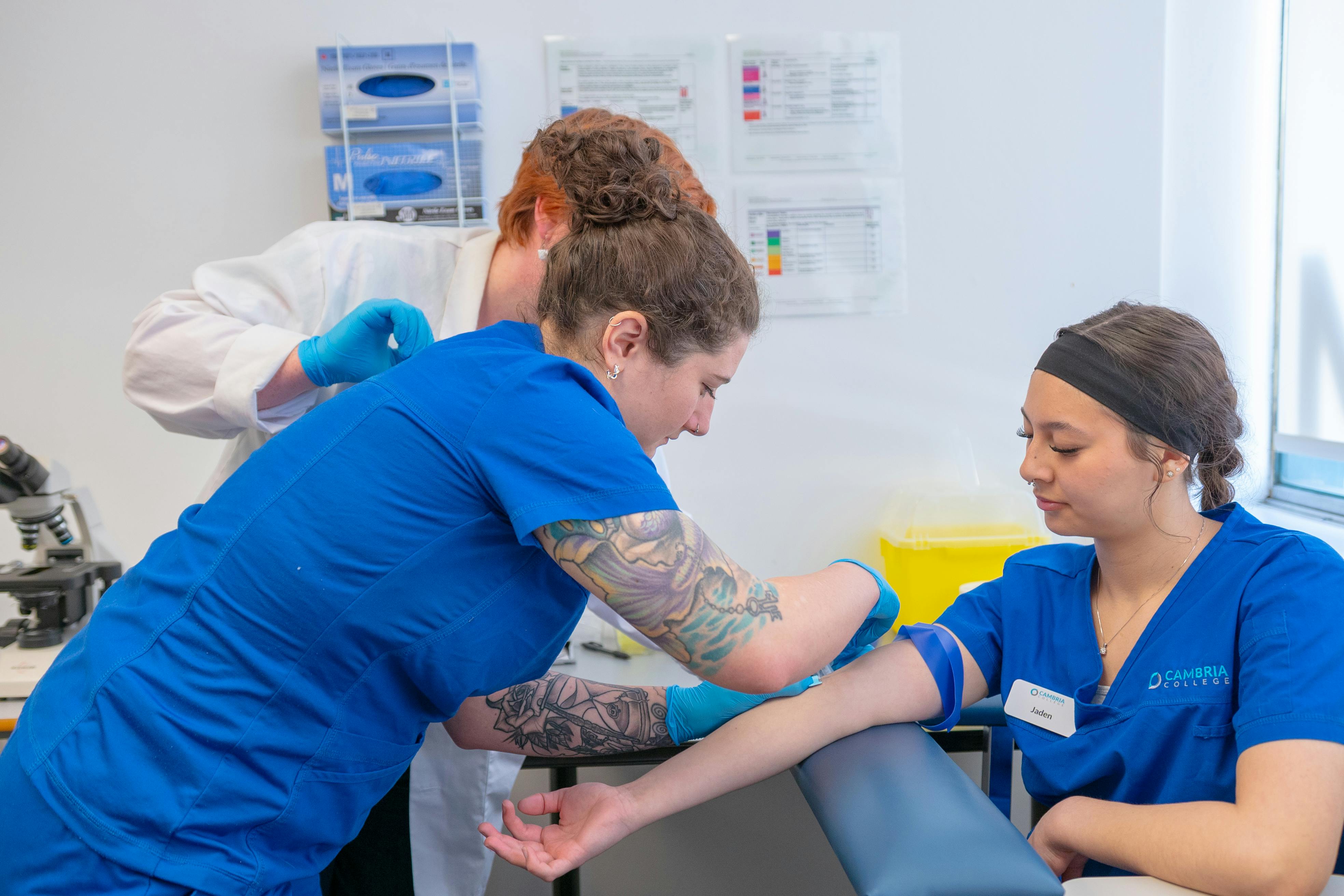 Students practicing blood draws on other students. Photo By Sahil Captures on Pexels.com.